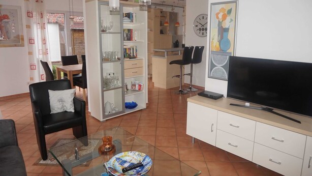 A living room with a TV, a glass coffee table, a bookshelf, and a dining area with chairs and a table.