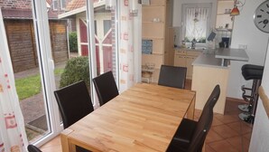 A dining area with a wooden table and chairs, a kitchen with a sink and cabinets, and a view of a garden through a sliding glass door.