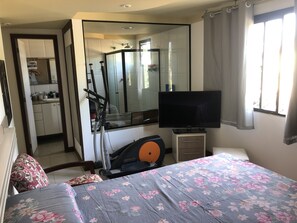 Quarto com cama, televisão, esteira e área de chuveiro.