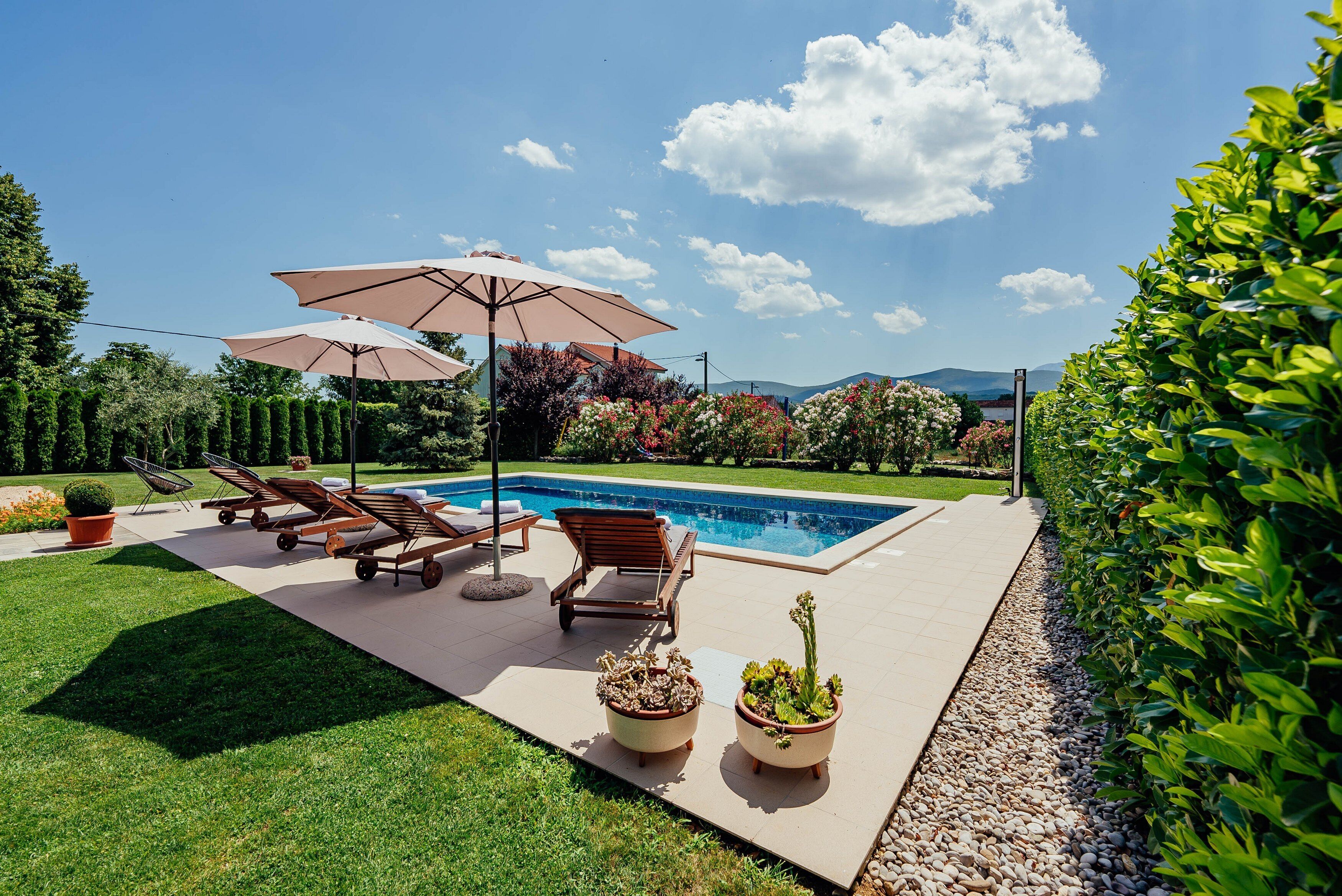 A poolside area with lounge chairs, umbrellas, and potted plants.