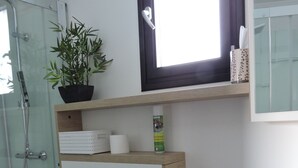 Een moderne badkamer met een douchecabine van glas, een wit toilet, een klein wastafeltje met een spiegel en een plank met toiletartikelen.