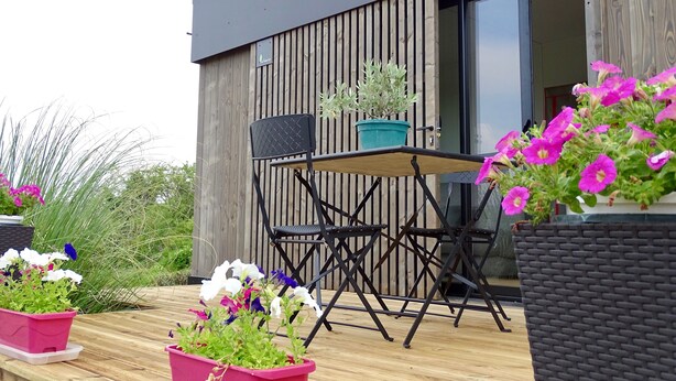Een modern zitgedeelte buiten met een tafel en stoelen, omringd door potplanten en bloemen.