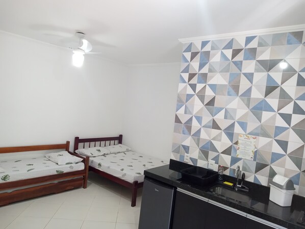 A small, clean room with two single beds, a black kitchen counter, and a geometric-patterned wall.