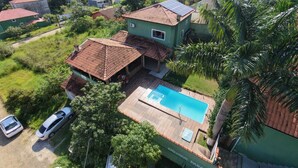 A residential property with a swimming pool, a car parked in front, and a view of surrounding hills. - Family house, with pool views of the mountains 7 minut from the center Penedo RJ (Itatiaia)