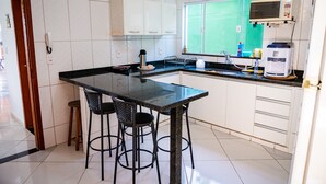 A modern kitchen with a black countertop, white cabinets, a built-in microwave, and a window with a green view. - Family house, with pool views of the mountains 7 minut from the center Penedo RJ (Itatiaia)