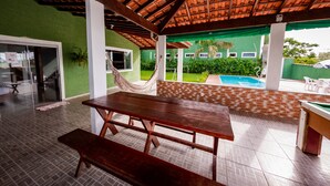 An outdoor covered patio with a wooden table and benches, a hammock, and a pool area. - Family house, with pool views of the mountains 7 minut from the center Penedo RJ (Itatiaia)