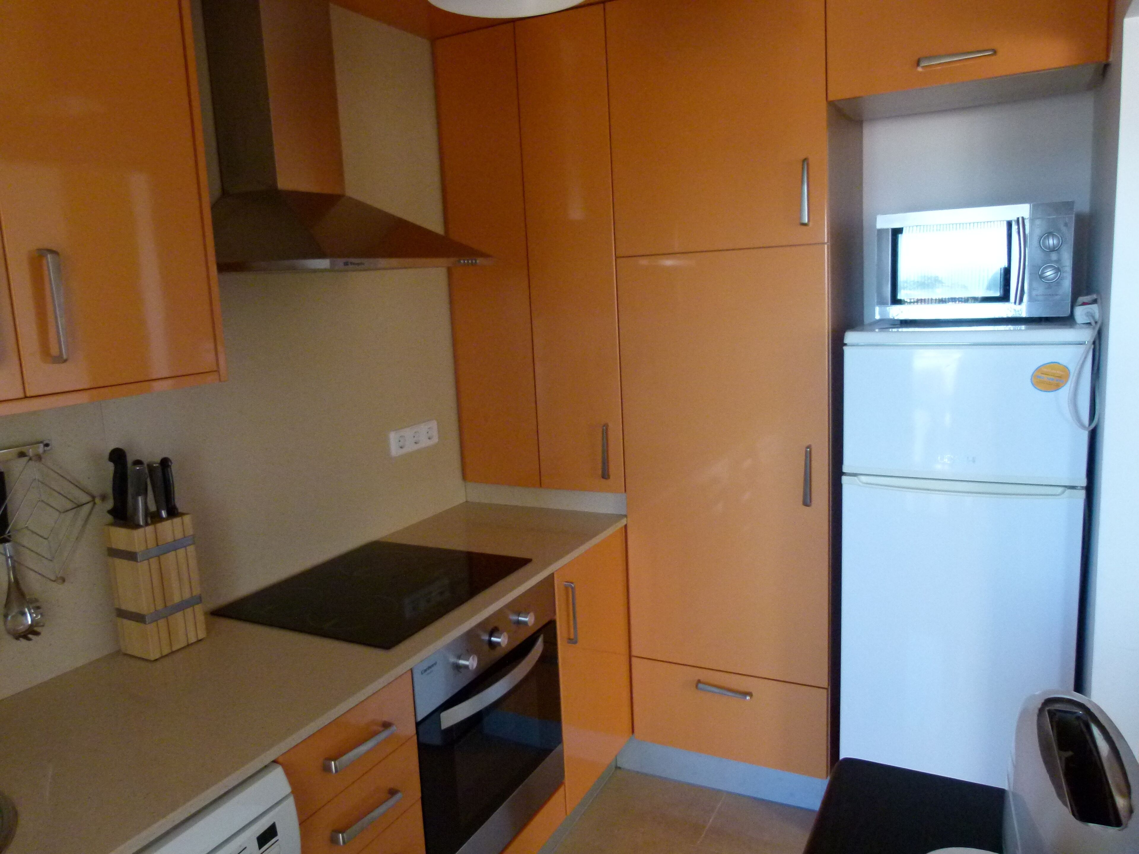 Una cocina compacta con gabinetes de madera, horno empotrado, microondas y pileta.