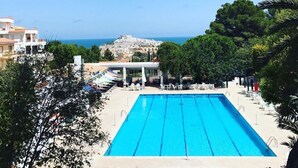 A rectangular swimming pool with clear blue water, surrounded by lounge chairs and umbrellas, with a view of a coastal town and the sea in the background. - Family friendly, parking, beach, high-speed wifi, excursions, sea view ... (Peñíscola)
