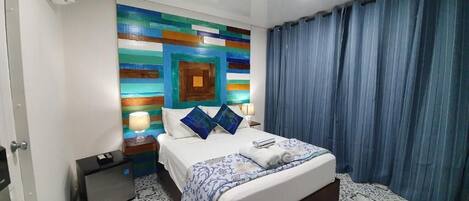 A hotel room with a bed, a nightstand, a lamp, and a wall with a colorful geometric pattern.