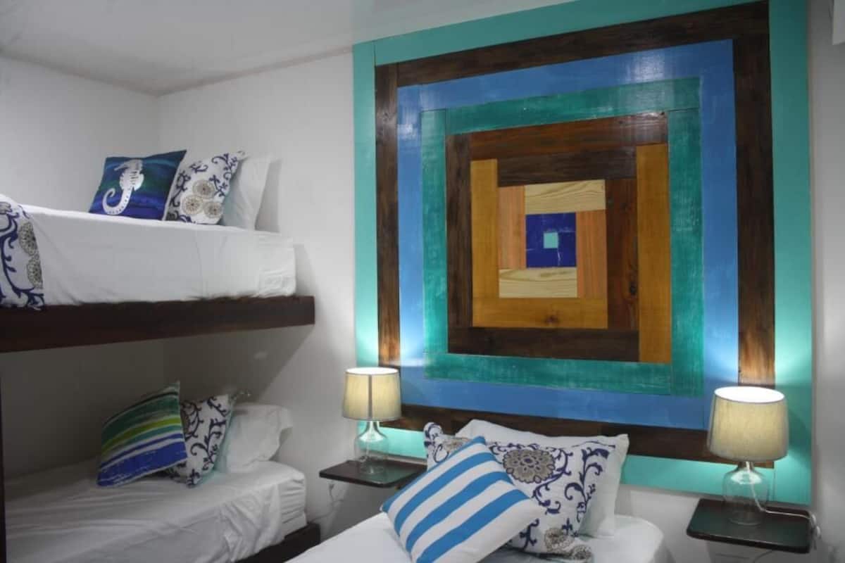 Quarto de hotel com beliches, um mural na parede e luminárias de cabeceira.