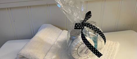 A toilet with a folded white towel on top and a plastic bag with a bottle and a black ribbon.