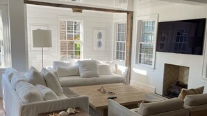 A spacious living room with a large white sofa, a wooden coffee table, and a fireplace. - 100 Steps to Main Street. 5 bedrooms and 6.5 baths. New and Completely renovated (Nantucket)