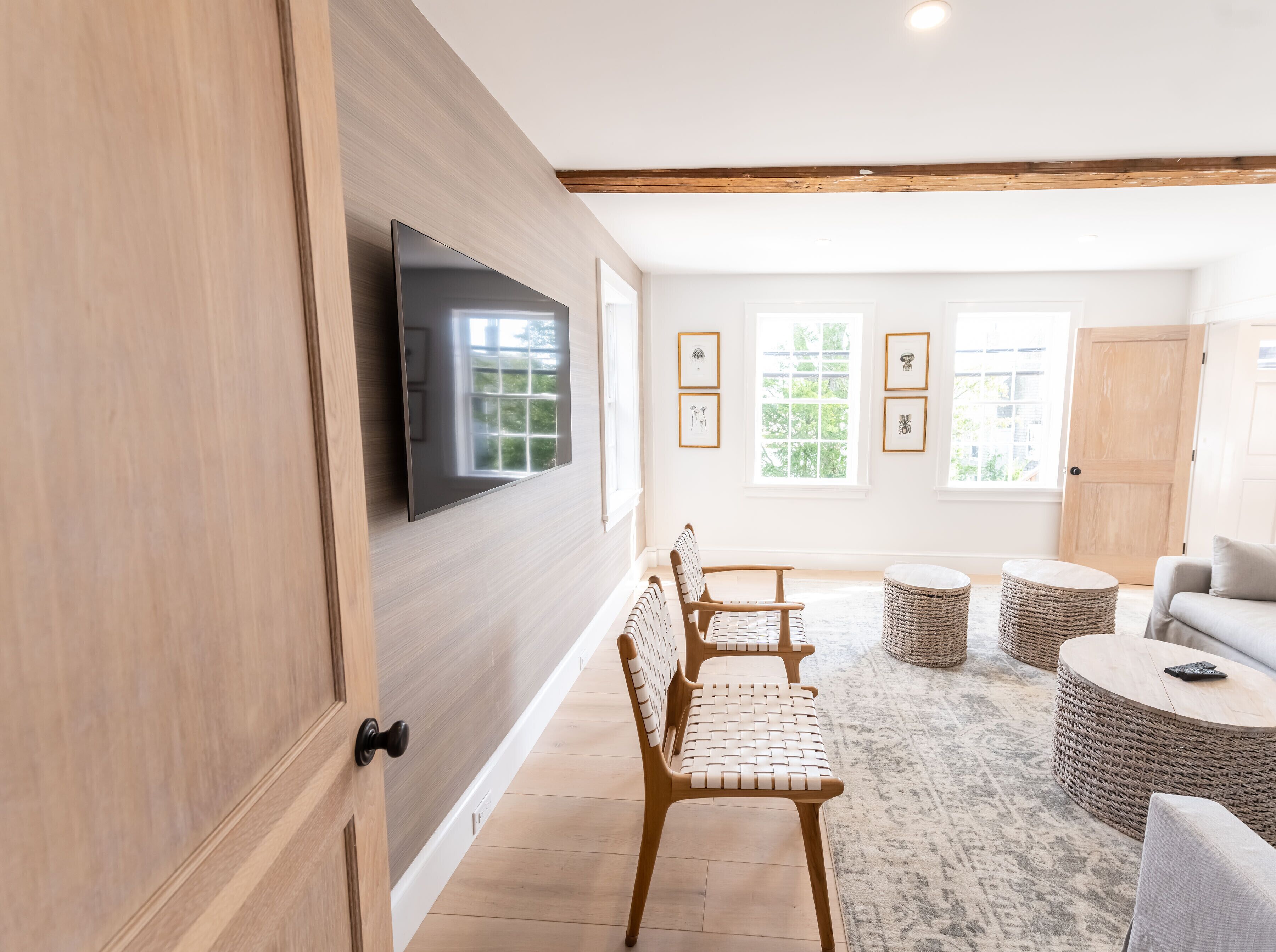 A modern living room with a flat-screen TV mounted on the wall, a wooden bench, a round coffee table, and a wicker ottoman.