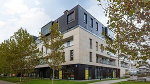 A modern multi-story building with a flat roof, large windows, and a paved walkway.