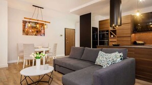 A modern living room with a grey sofa, a round coffee table, and a dining area with chairs and a table.