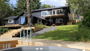 Een modern huis met een jacuzzi, houten terras en gazon.