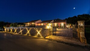A well-lit residential property with a stone wall, a gated entrance, and a clear night sky.