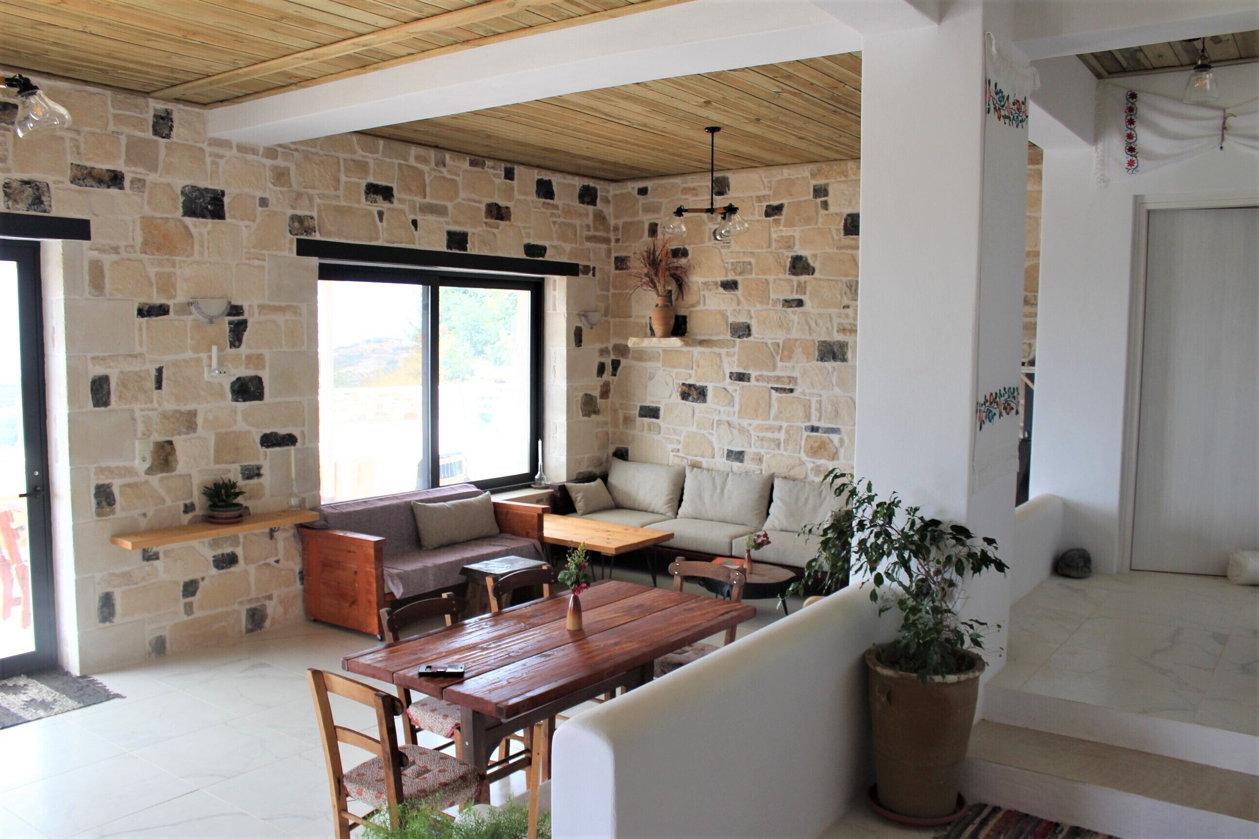 Un salón amplio con pared de piedra, techo de madera y una variedad de opciones de asiento, incluyendo un sofá, sillas y una mesa.