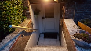 Eine Treppe führt zu einer Tür, begleitet von einem Geländer, Kies und Pflanzen.