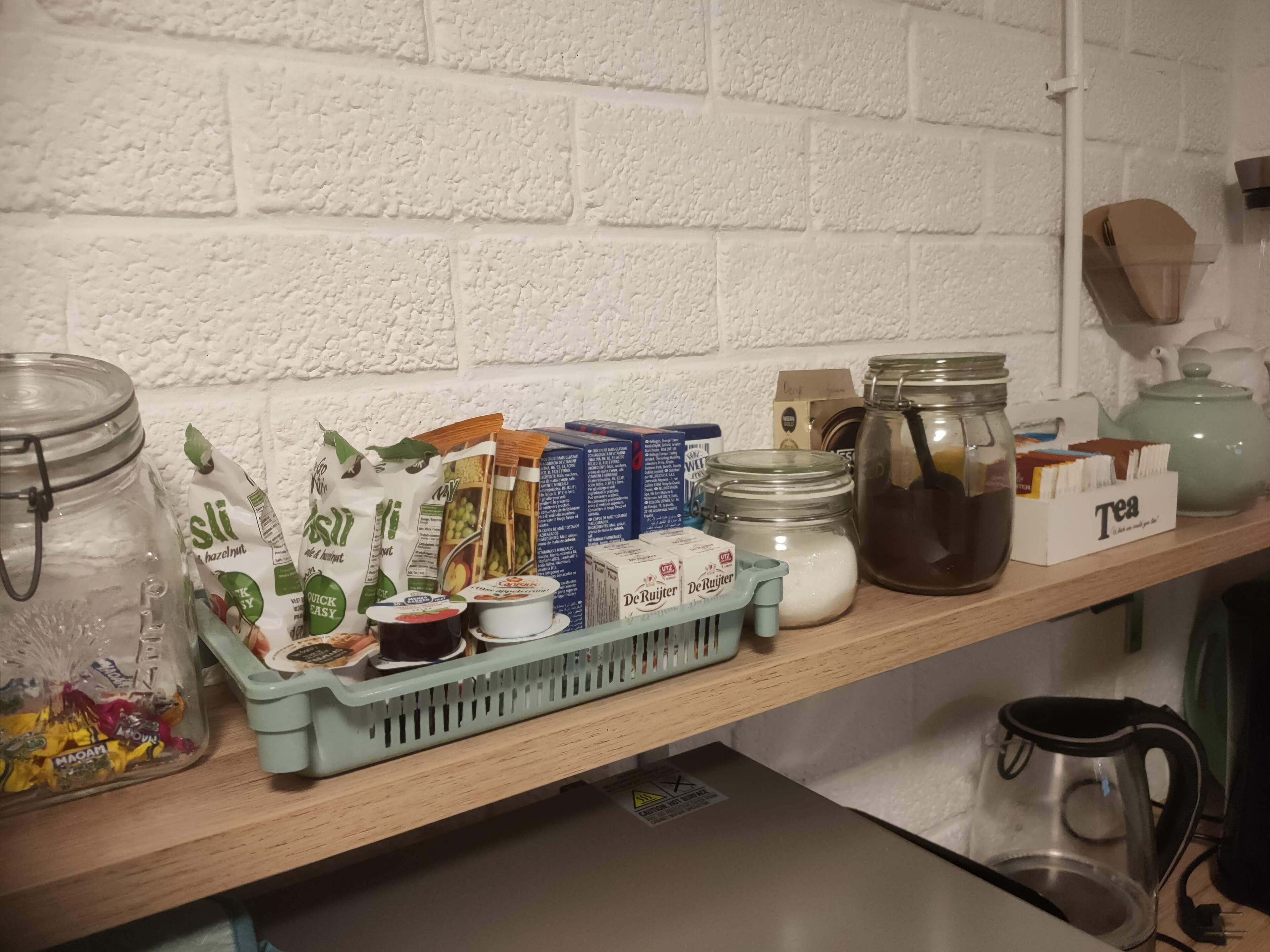 A kitchen shelf with various food items and containers, including jars, boxes, and a kettle.