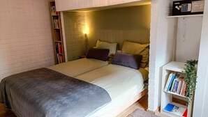 Ein gemütliches Schlafzimmer mit Bett, Nachttischen, einem Bücherregal und einer kleinen Pflanze.