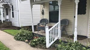 Une maison avec un porche, une porte d’entrée et un petit jardin agrémenté de plantes et d’un chemin.