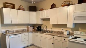 Une cuisine avec des meubles blancs, un plan de travail en granit, un lave-vaisselle, une cuisinière et un four à micro-ondes.