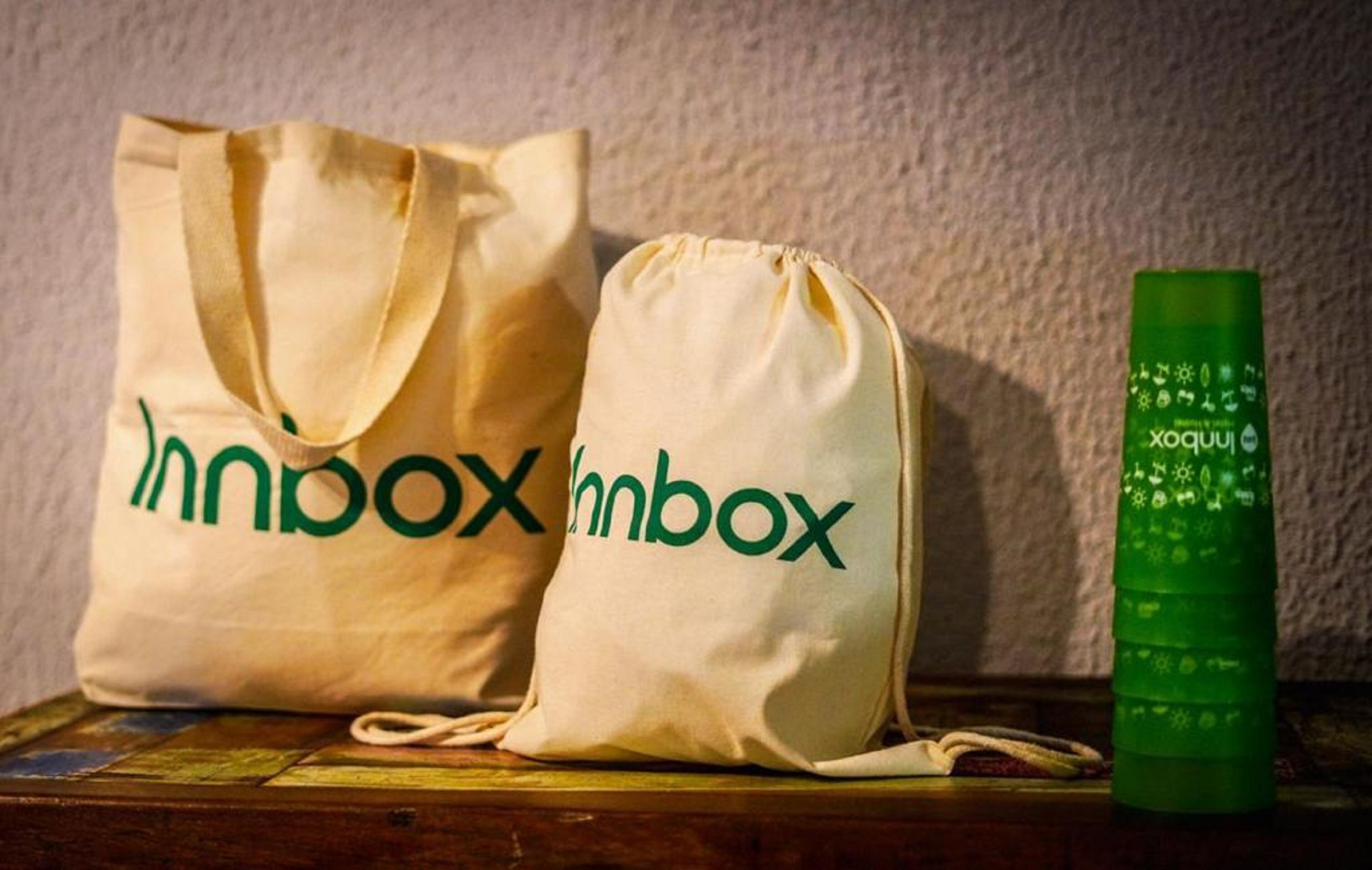 Two bags with "Inbox" branding, a green bottle, and a wooden surface.