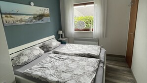 Un dormitorio con cama, mesita de noche, lámpara, ventana con cortinas e iluminación en el techo.