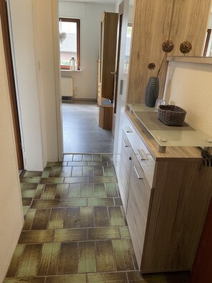 Un pasillo con piso de baldosas que conduce a una cocina con armarios de madera y encimera.