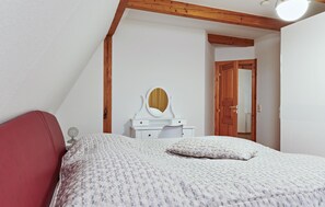 A bedroom with a bed, a dresser with a mirror, and a door leading to another room.