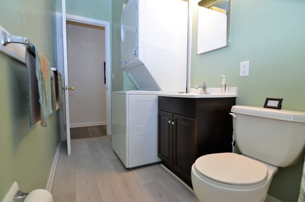 Une petite salle de bain avec des toilettes blanches, un lavabo avec un miroir et un lave-linge.