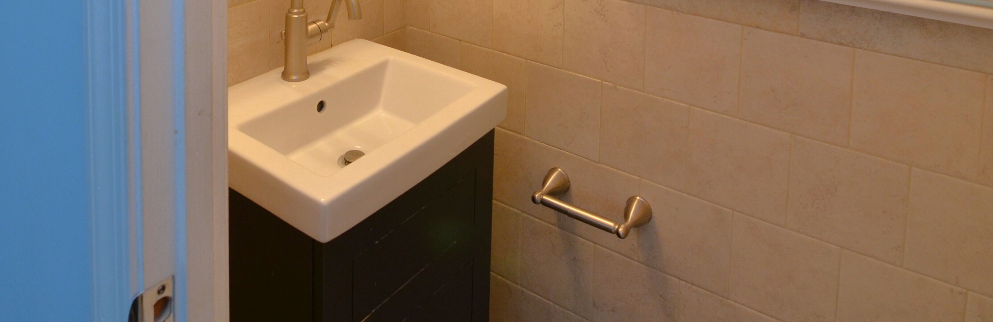 Une salle de bain avec un lavabo blanc, un porte-serviettes et des murs recouverts de carreaux beiges.