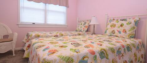 A pink bedroom with two beds, a chair, and a window with blinds.