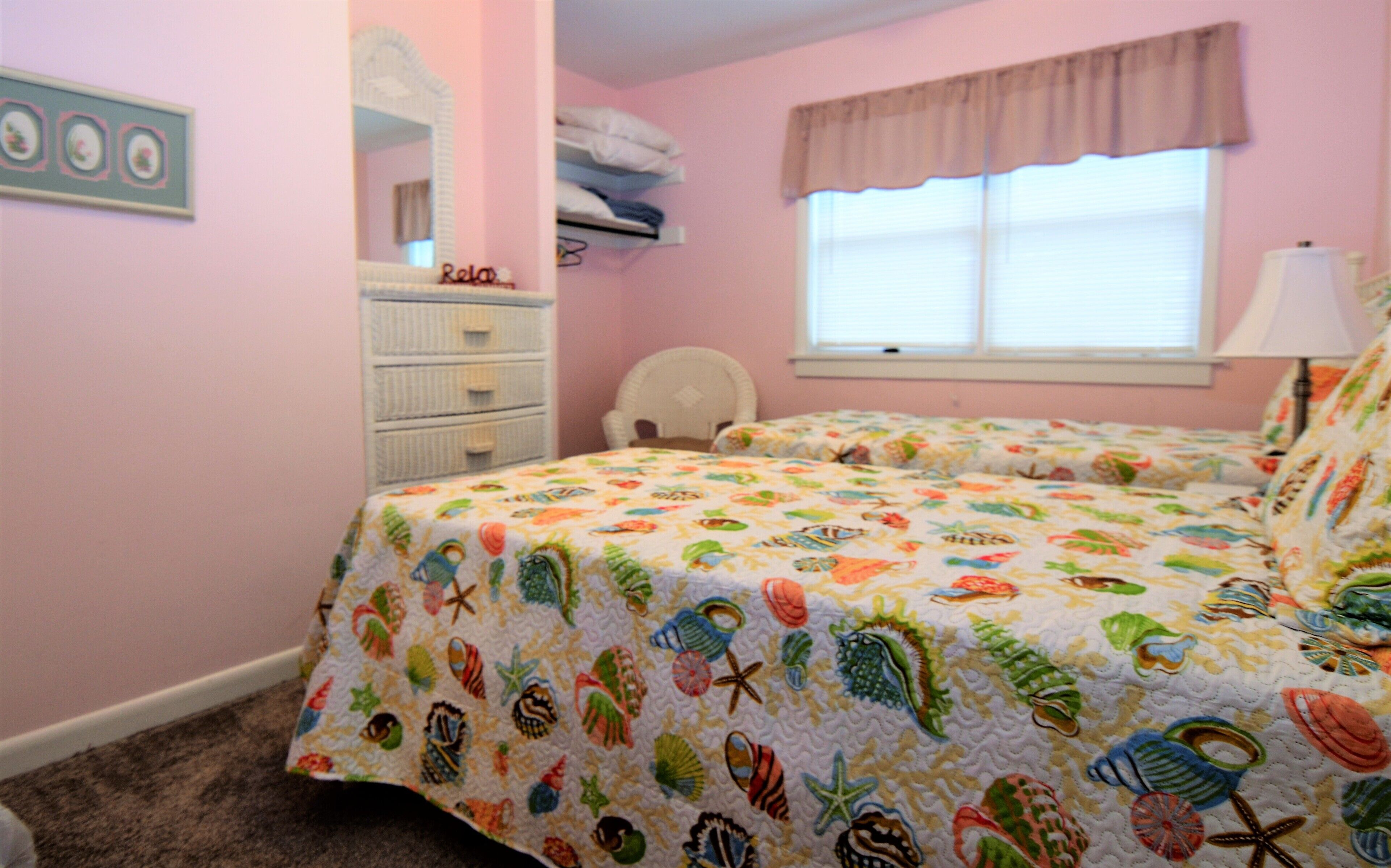 A bedroom with two beds, a dresser, a chair, a window with blinds, and a mirror.