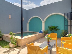 A courtyard with a pool, yellow chairs, and potted plants.