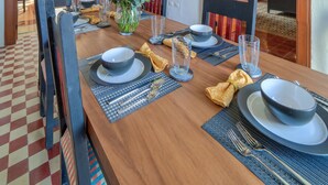 Een eetruimte met een houten tafel gedekt voor vier personen, omringd door stoelen. In de achtergrond is een kast met glazen deuren te zien.