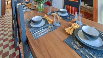 Un coin repas avec une table en bois, dressée pour quatre personnes, entourée de chaises. On aperçoit un meuble avec des portes en verre à l’arrière-plan.