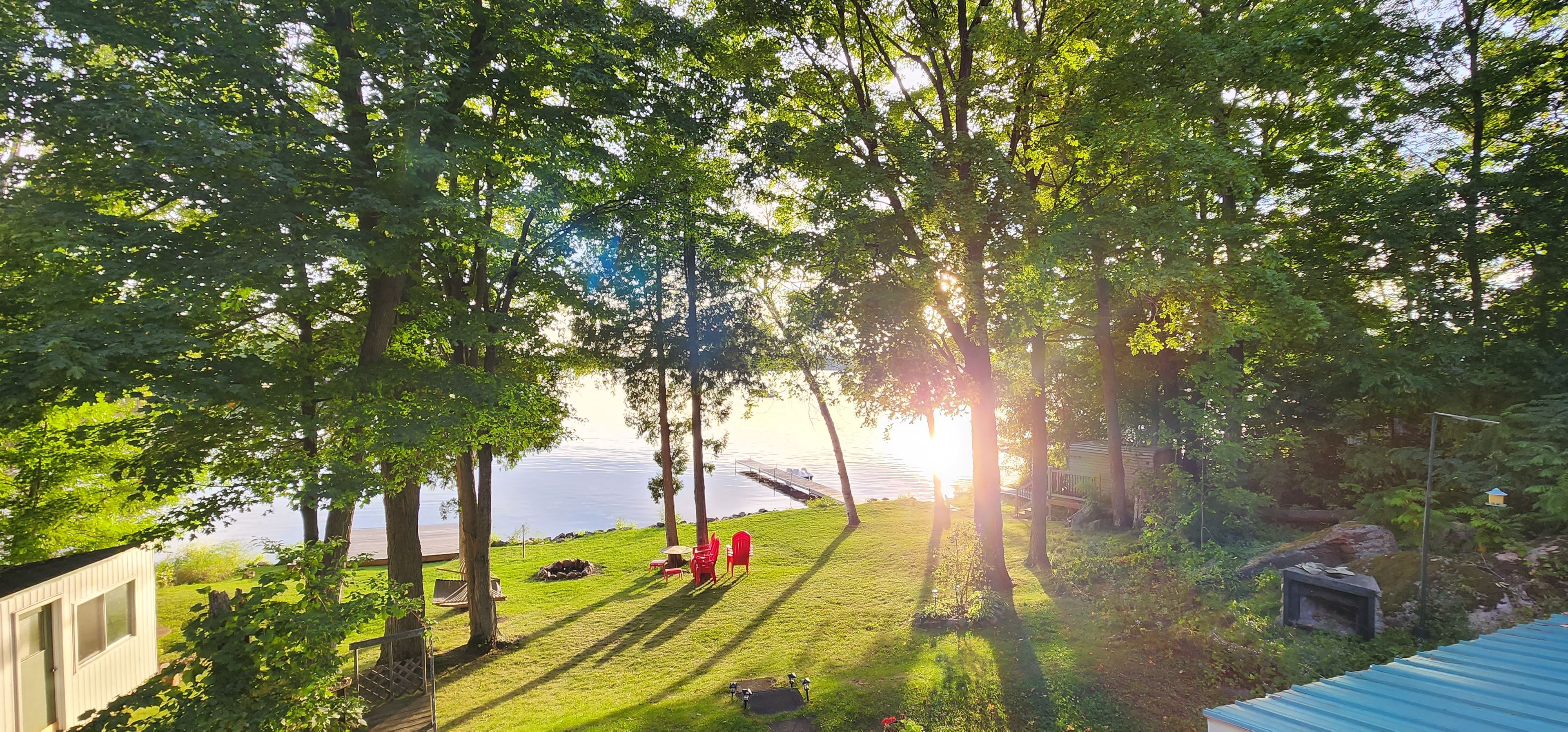 A lakeside view with a grassy area, a wooden deck, and a small building with windows.