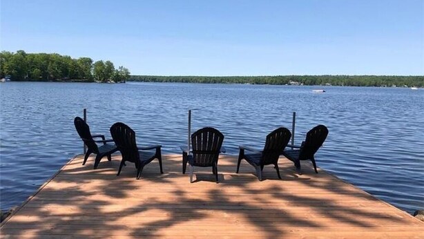 Une jetée en bois avec trois chaises, donnant sur un lac paisible.