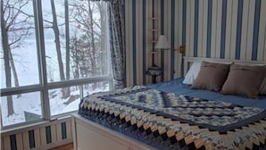 Une chambre avec une grande fenêtre, un lit recouvert d’une courtepointe à motifs et une table de chevet avec une lampe.