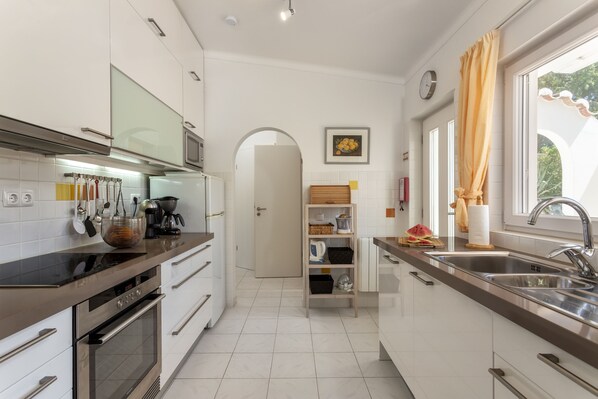 Una cocina moderna con electrodomésticos de acero inoxidable, armarios blancos y un amplio ventanal con cortinas.