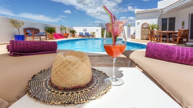 Ein Poolbereich mit Liegestuhl, Strohhut und Cocktailglas mit Trinkhalm.