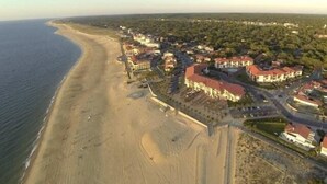 Vista aérea de uma área costeira com uma praia de areia, edifícios residenciais e céu claro.