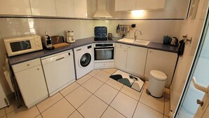 Cucina compatta con forno a microonde, tostapane, lavatrice, forno, lavello e piccolo cestino.