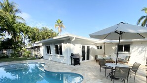 Ein Poolbereich mit Grill, Sitzgelegenheiten und Palmen.
