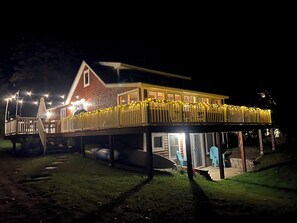 Una casa a due piani con veranda coperta, illuminazione esterna e garage visibile.
