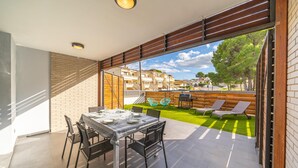 A patio with a table set for dining, a grassy lawn, and a view of neighboring buildings. - Elvira: Pleasant house with communal pool located in a quiet area (L'Escala)