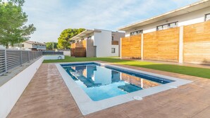 A modern residential pool area with a rectangular pool, surrounded by a wooden deck and a paved walkway. - Elvira: Pleasant house with communal pool located in a quiet area (L'Escala)