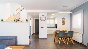 A modern living space with a staircase, a dining area with a table and chairs, a kitchen in the background, and a wall clock. - Elvira: Pleasant house with communal pool located in a quiet area (L'Escala)